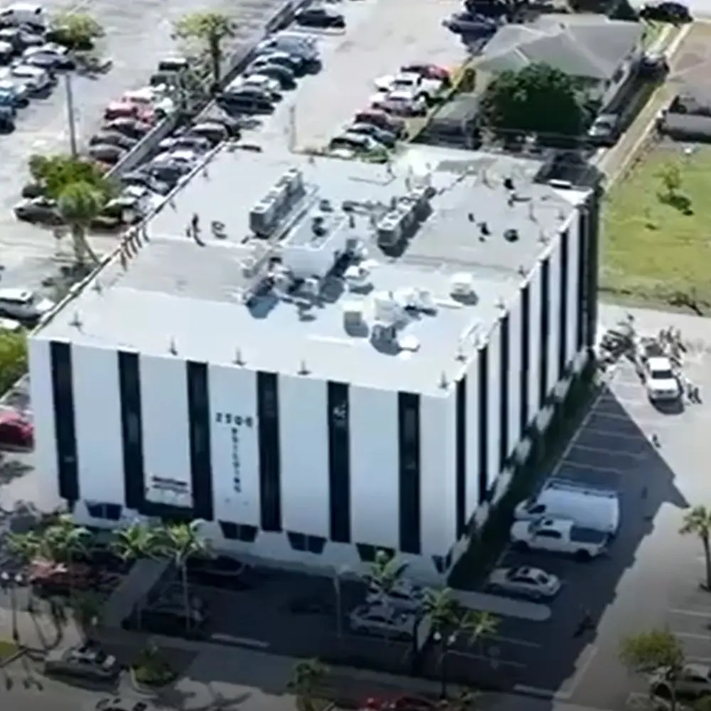 Aerial view of a commercial building featuring a newly installed TPO roofing system, surrounded by parking lots, palm trees, and neighboring structures. Perfect example of professional TPO roof installation for energy efficiency and durability.